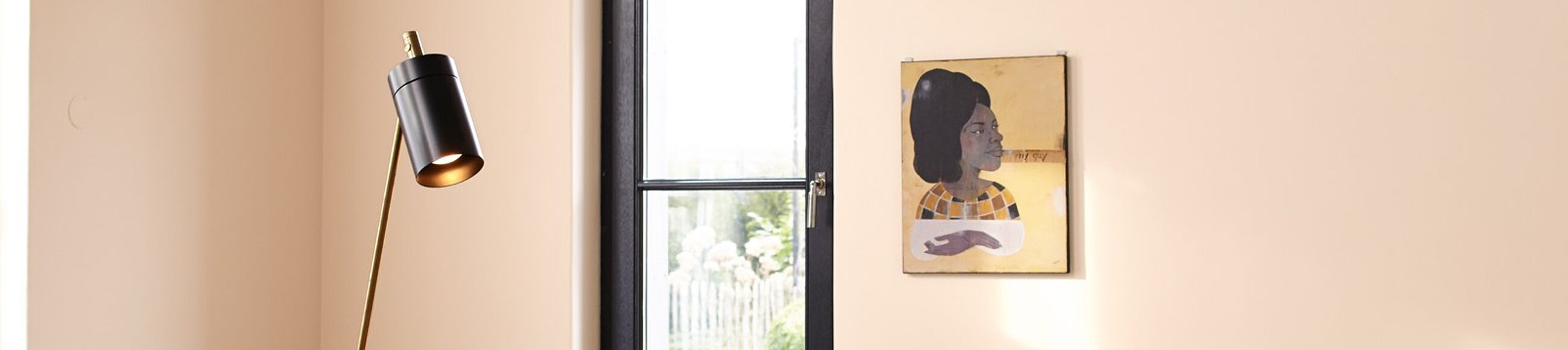 Schwarze Stehlampe vor Wand in hellem Apricot mit dunkelbraunem Sprossenfenster.