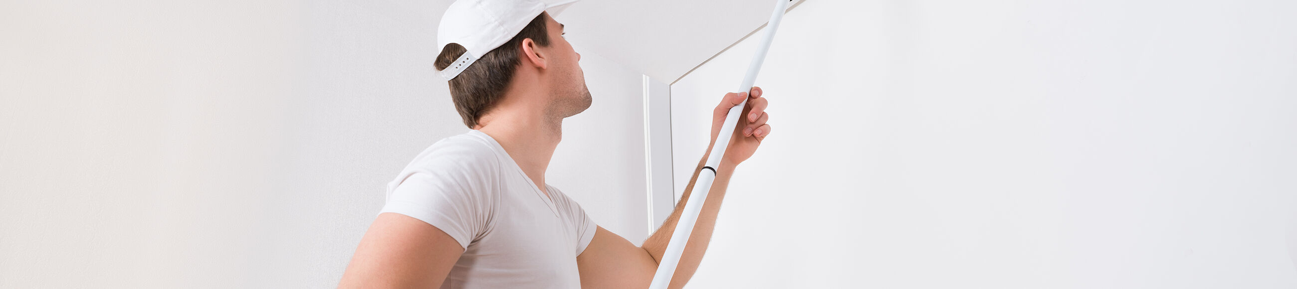 Mann streicht Decke mit weißer Farbe