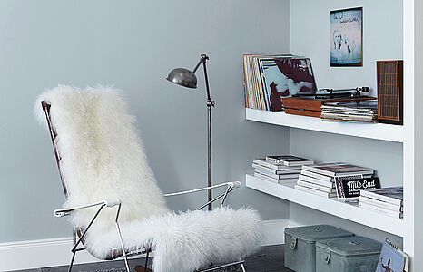 Elegantes Blaugrau. Ein in diesem hellen und luftigen Farbton gestrichenes Wohnzimmer mit Wandregalen und Lesesessel.