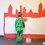 Eine Wand wird von einem kleinen Jungen mit Orange in Form einer Stadtsilouhette angemalt.