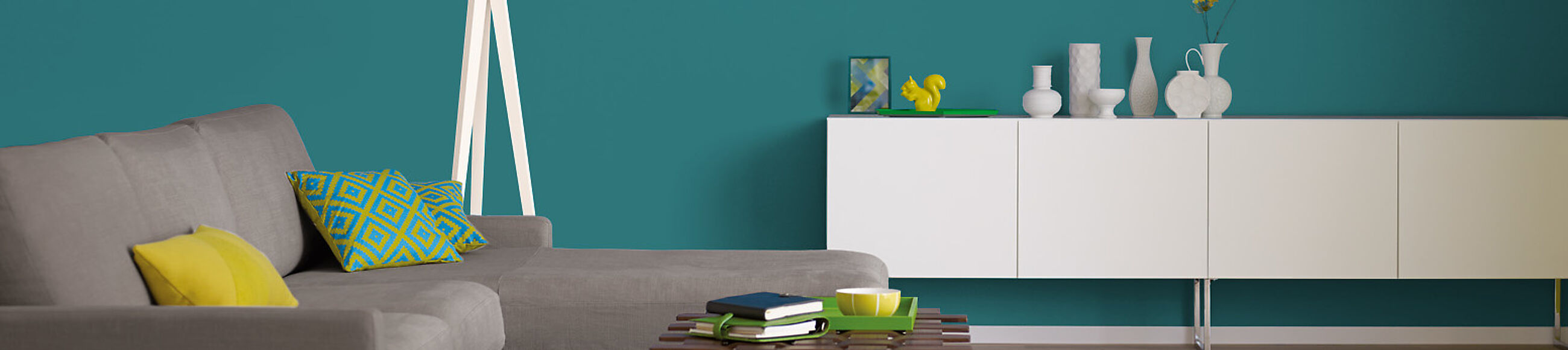 Ein Graues Sofa, ein weißes Sideboard und Deko-Objekte vor einer Wand in Petrol