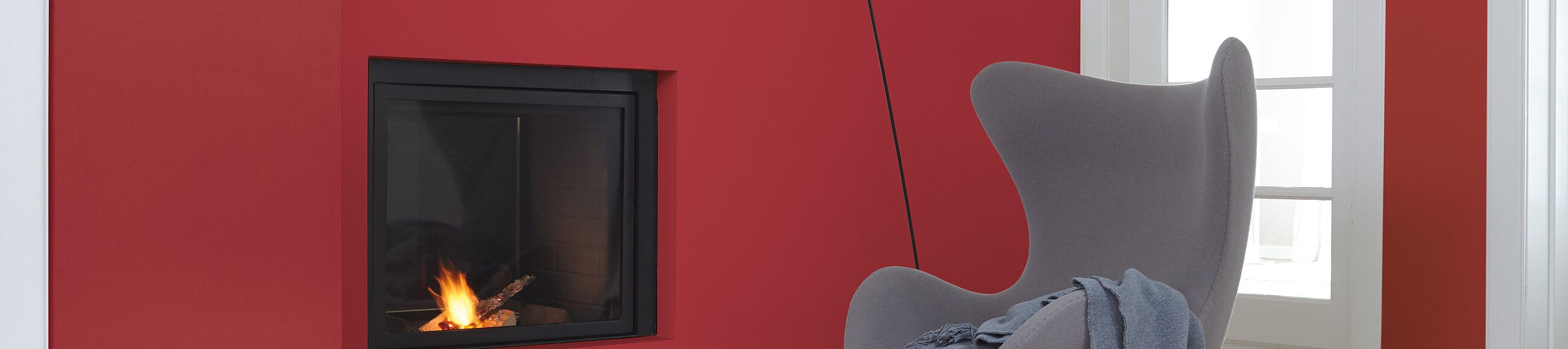 Grauer Sessel mit Hocker vor roter Wand mit eingelassenem Kamin 