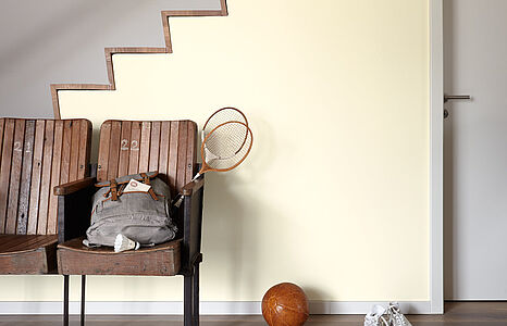 Helles Lichtgelb. Ein in diesem sanft leuchtenden Farbton gestrichener Flur mit Treppenaufgang und Holzbank mit Klappsitzen.