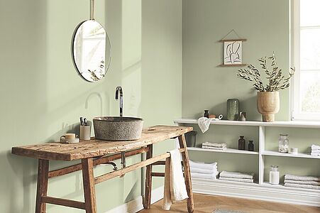 Weiches Pastellgrün. Ein in diesem umschmeichelnden Oliv-Ton gestrichenes Badezimmer mit Waschtisch aus rustikalem Holz.