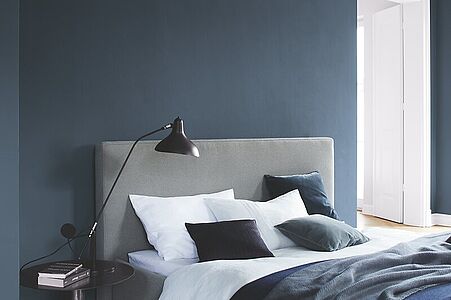 Tiefes Mitternachtsblau. Ein in diesem festlichen und royalen Dunkelblau gestrichenes Schlafzimmer mit einem hellgrauen Bett.