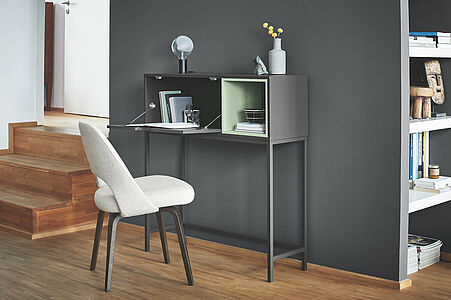 Expressives Graphitgrau. Ein moderner, grauer Sekretär mit Polsterstuhl vor einer in diesem zeitlosen Grau gestrichenen Wand.