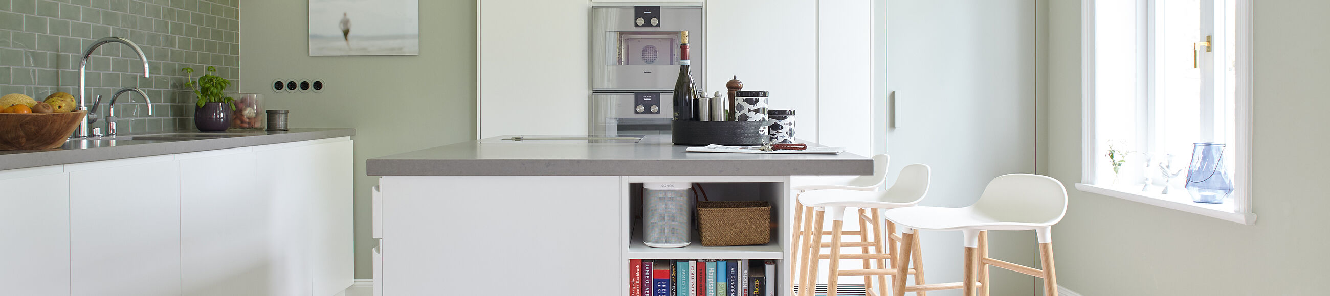 Helle Küche mit Kücheninsel in der Mitte, zwei Barhockern und weißen Küchenschränken