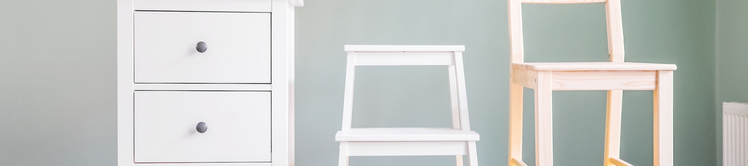 Eine weiße Kommode, ein weißer Tritthocker und ein Holzstuhl