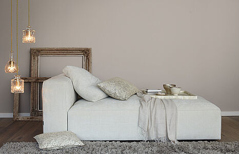 Romantisches Taupe. Ein in diesem noblen Graubraun gestrichenes Wohnzimmer mit einer modernen, hellgrauen Ottomane.