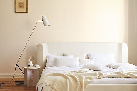 Warmes Lichtweiß. Ein in diesem vornehmen und natürlichen Farbton gestrichenes Schlafzimmer mit beigem Bett und Stehlampe.