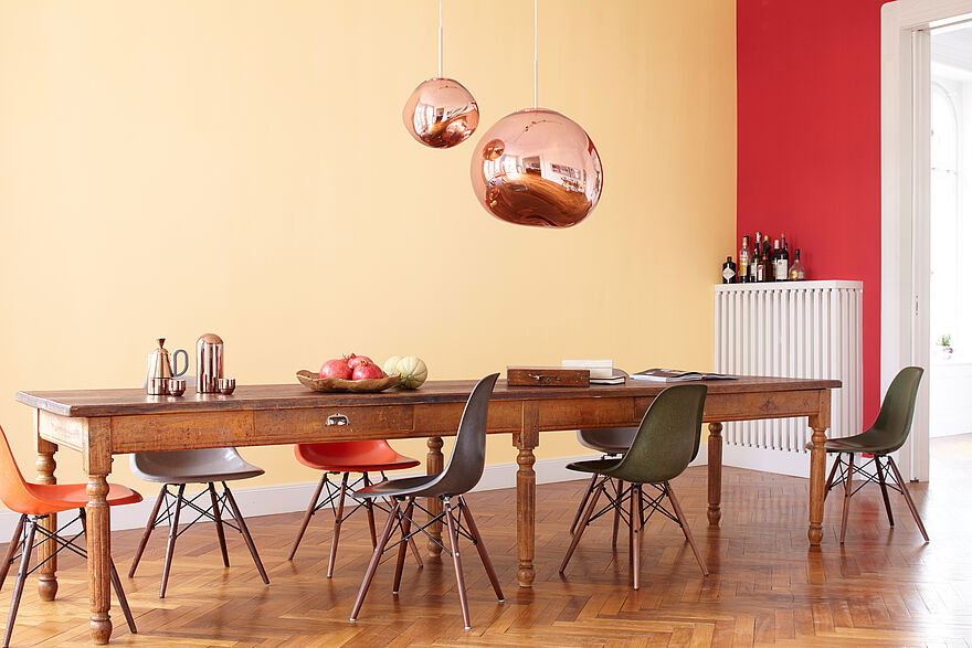Warmes, gemütliches Esszimmer mit Holztisch und Messinglampen vor einer orange roten Wand in der Alpina Farbe Granatapfel und Sweet Home.