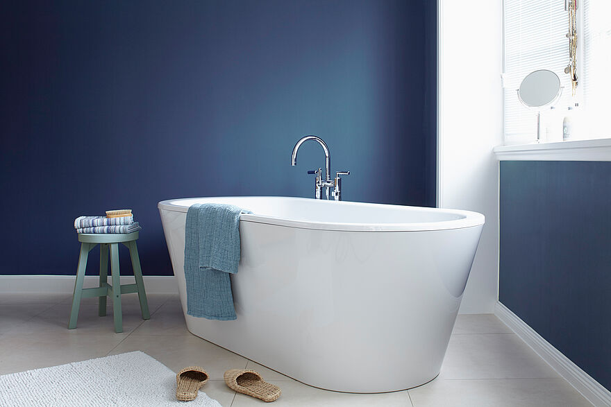 Weißes, modernes Badezimmer mit freistehender Badewanne und dunkel blauer Wand in der Alpina Farbe Blaue Stunde.