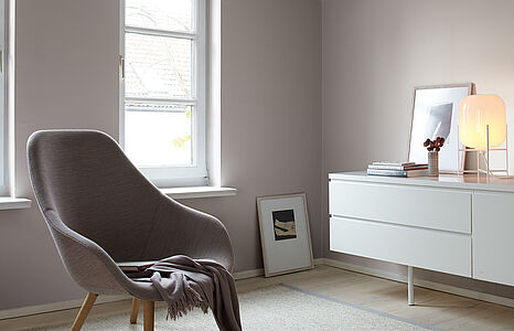 Würdevolles Hellgrau. Eine in diesem warmen, sanften Grau-Ton gestrichene Wand, davor ein weißes Sideboard und ein Sessel.