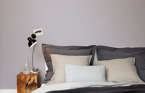 Graziles Graulila. Ein Bett mit mehreren Kissen vor einer in diesem kühlen und anziehenden Farbton gestrichenen Wand.
