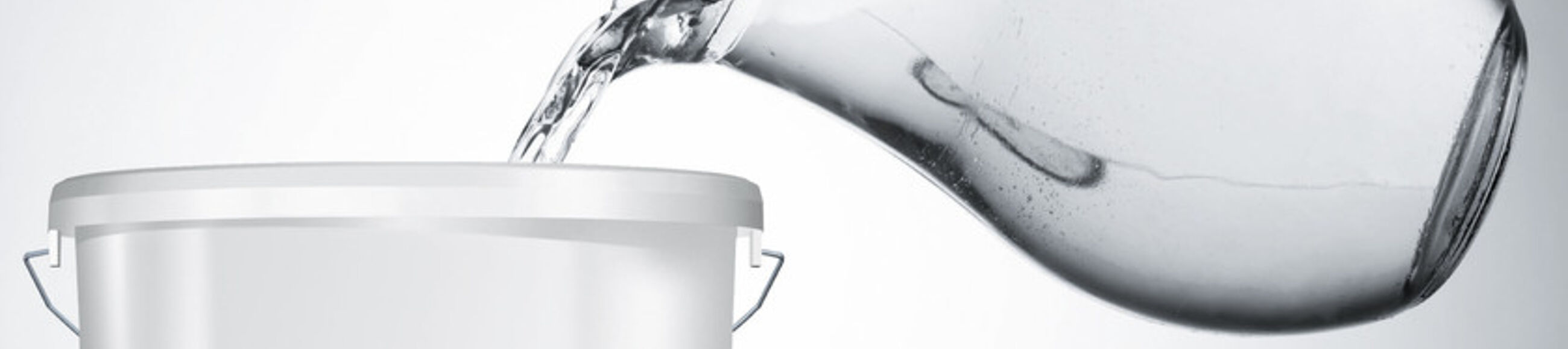 Wasser wird aus Glaskaraffe in Farbeimer geschüttet