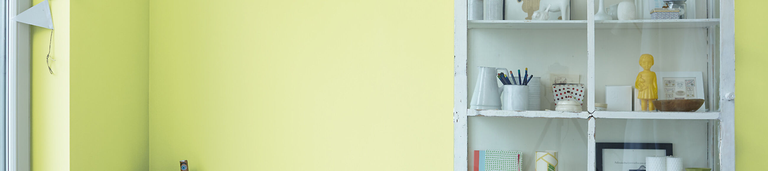 Weiße Vitrine mit Dekoobjekten vor hellgrüner Wand.