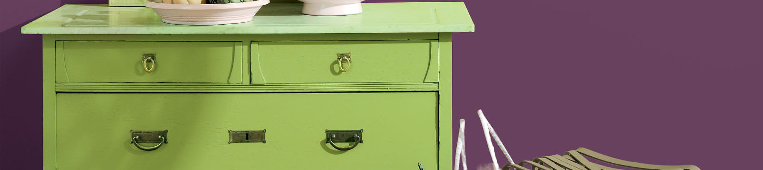 Eine grün lackierte Kommode vor einer violetten Wand