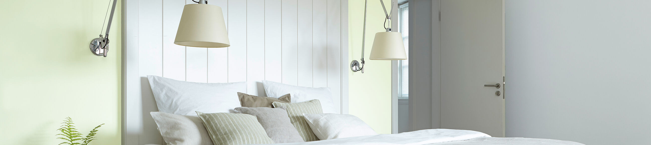 Ein großes Bett in einem hellen Raum vor einer gelben Wand