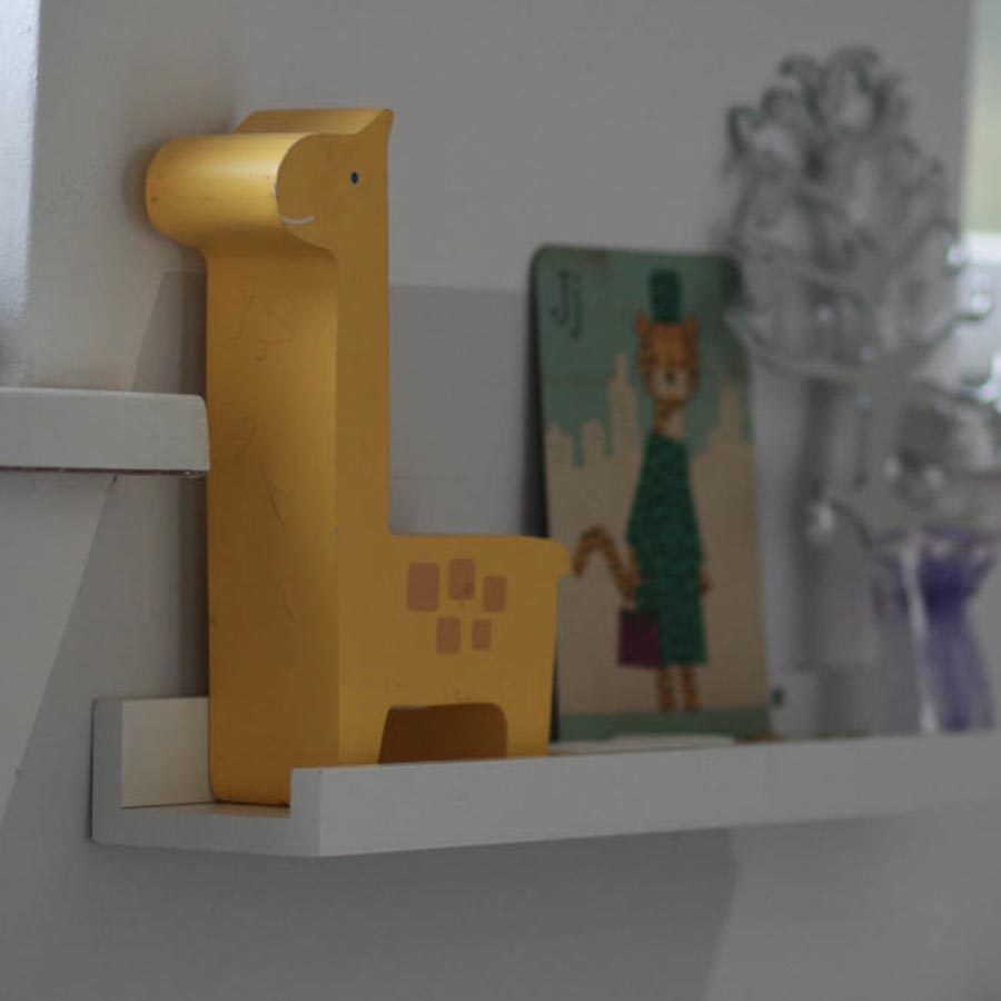 Eine graue Wabe hinter einem weißen Regal auf welchem Fotos und eine gelbe Holzgiraffe steht. 