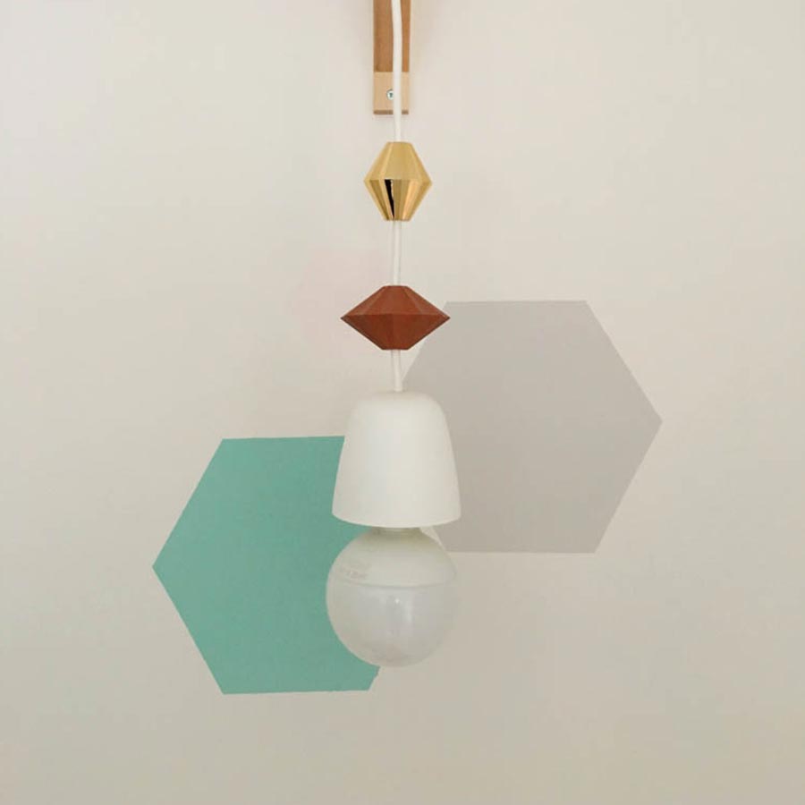 Eine Hängelampe vor türkischer und grauer Wanddekoration.