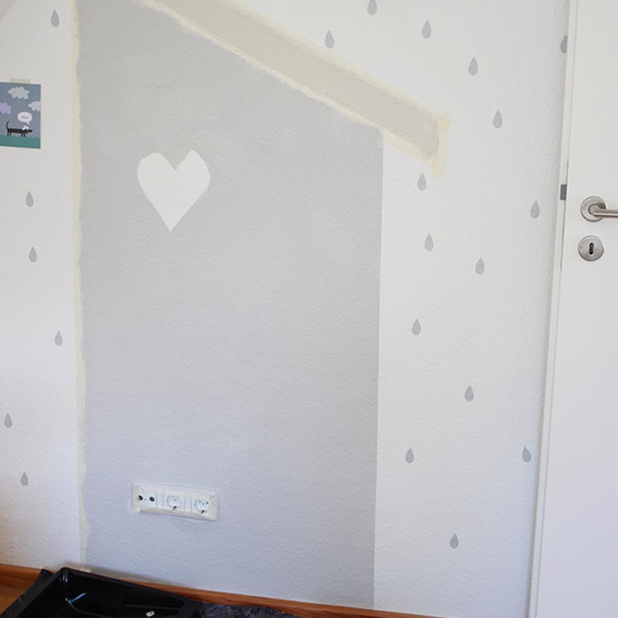 Eine weiße Wand wird mit grauen Tropfen und Herz verschönert.