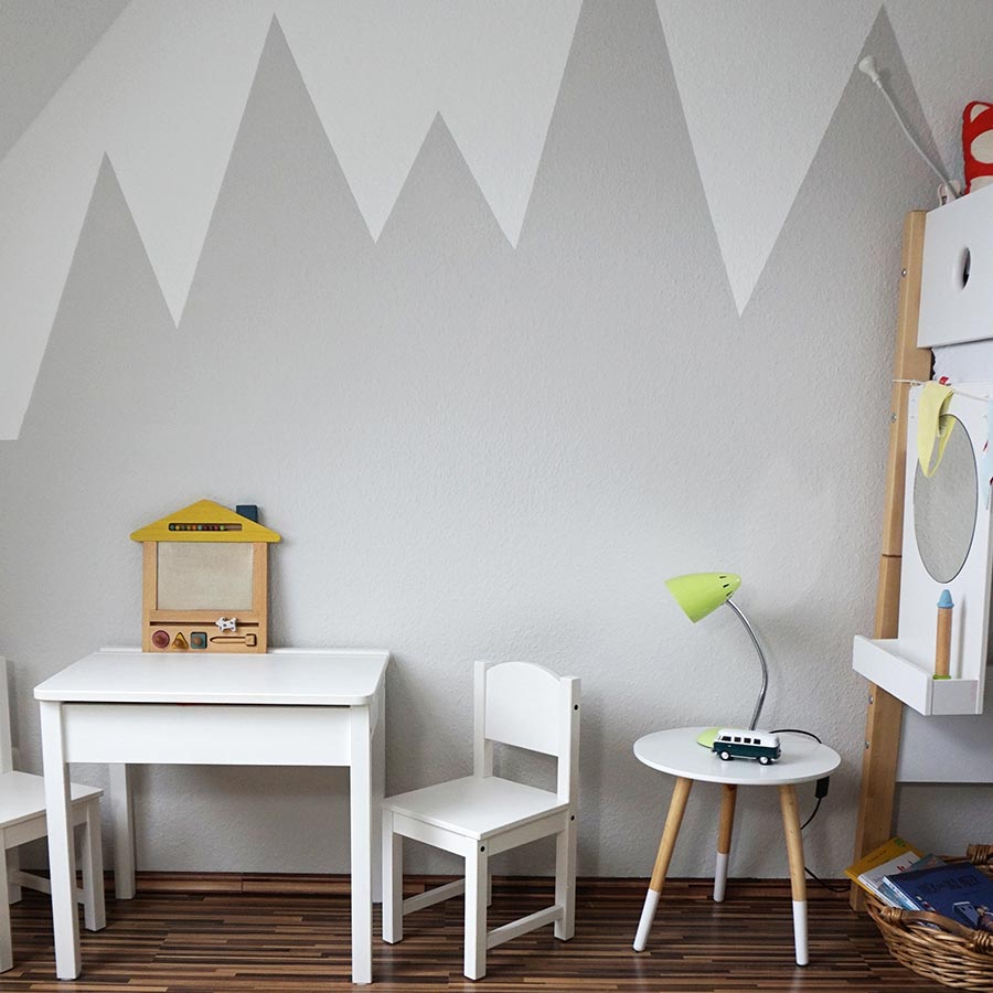 Kinderzimmer mit dunklem Holzboden, weißen Möbeln und grauen Bergen als Wanddekoration.