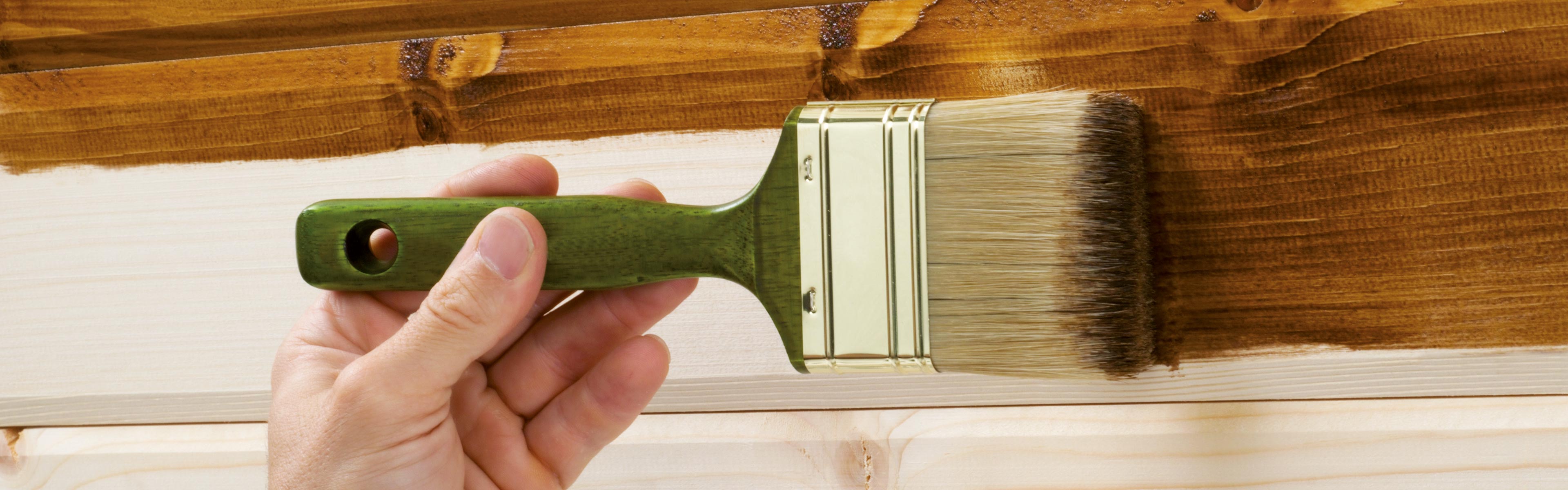 Eine Person lasiert eine Holzwand